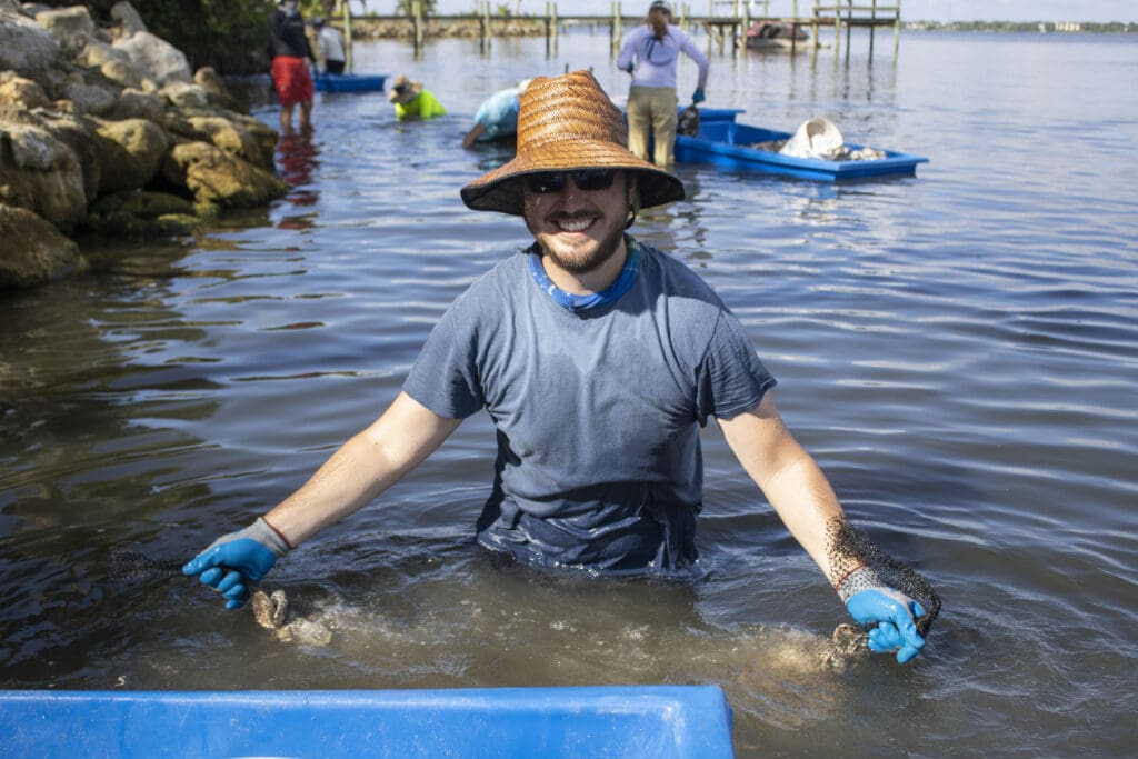 man smiling holding oyster mat that is being installed in the lagoon